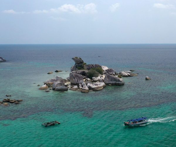 An aerial shot of a rocky island near a boat in the sea